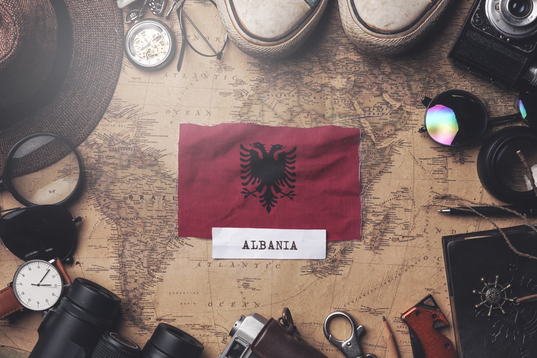 Albanian flag between traveler's accessories on old vintage map