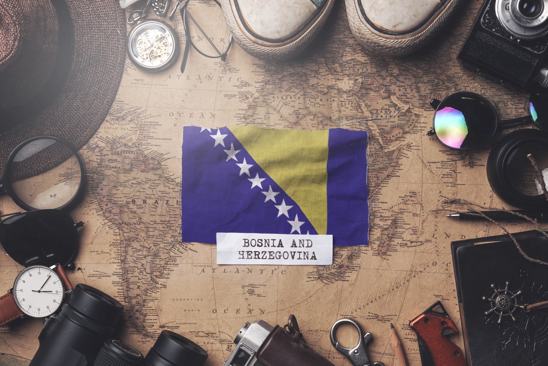 Bosnia and Herzegovina flag between traveler's accessories on old vintage map