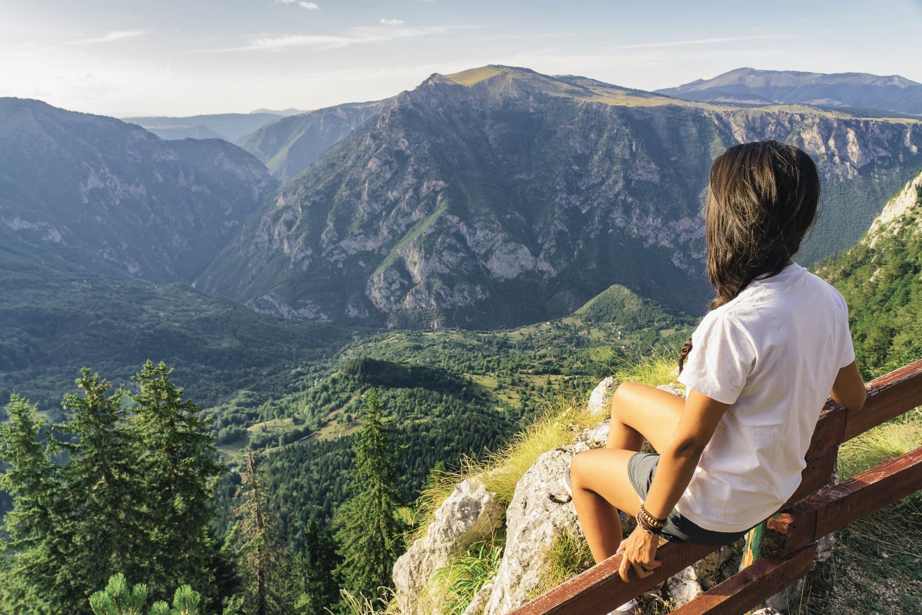 Girl sitting on wooden fence surrounded by hugh peaks of Durmitor Mountain Montenegro