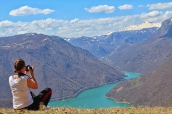 A girl photographs Piva Lake from a slope
