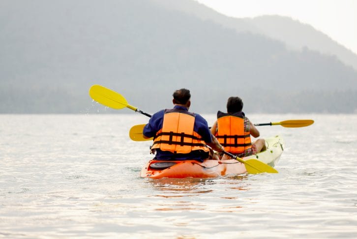 Man and woman swim on the kayak in the sea in the background of the island.