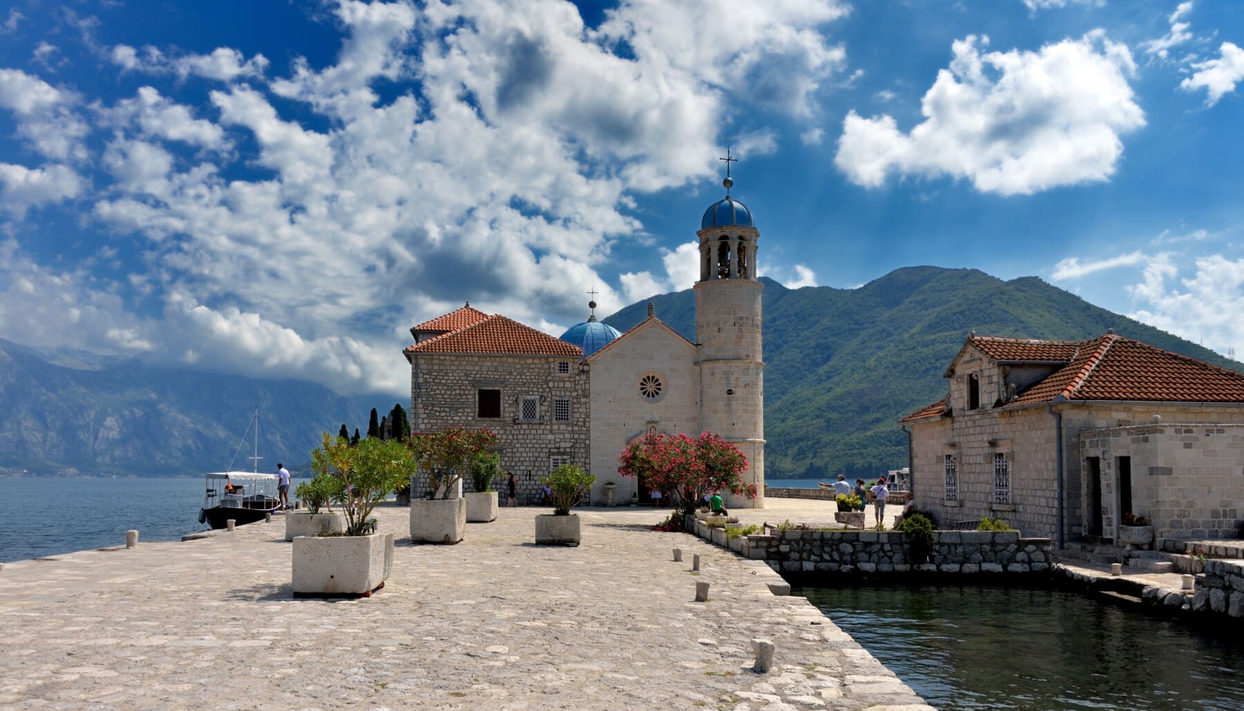the church of our lady of the rocks on a blue sky with clouds and mountains montenegro adventure