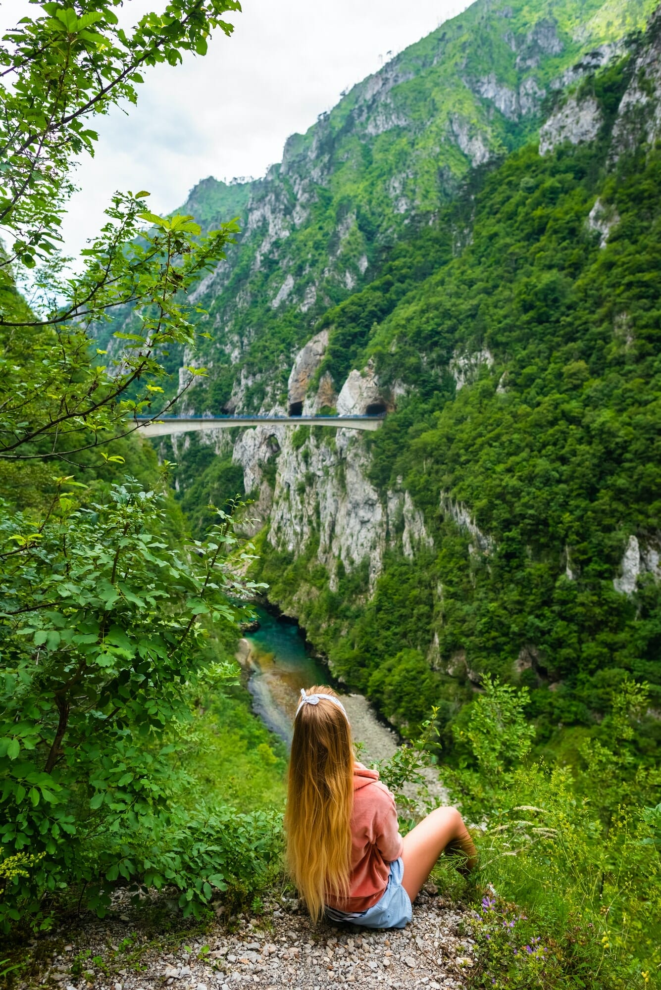 back view of woman looking at bridge between mountains above Piva River in Piva Canyon in Montenegro
